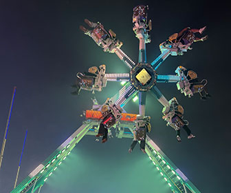 Lunarix, a brightly lit spinning amusement ride, seen from below at night, with riders suspended in seats.