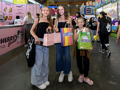 Three young girls hold shopping bags inside a busy Showbag Pavilion at the Sydney Royal Easter Show.