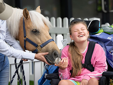 A young girl in a wheelchair smiles while feeding a pony at the Sydney Royal Easter Show.